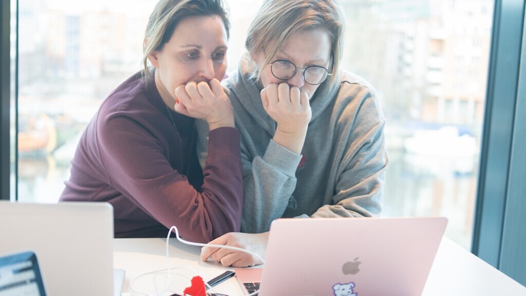 Två kvinnor sitter vid ett bord och tittar på en bärbar dator.