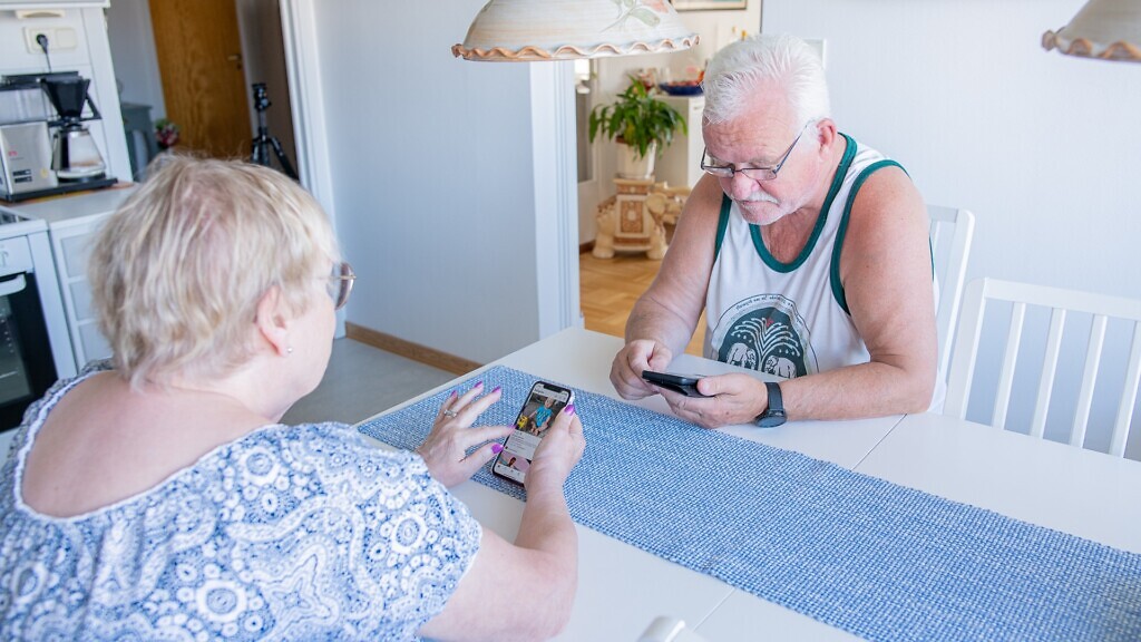 En man och en kvinna sitter vid ett bord och tittar på en mobiltelefon.